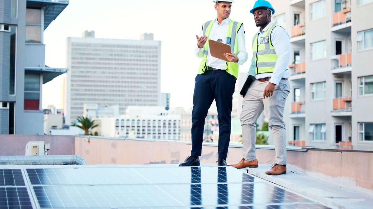 Ingenieros de pie en techo de edificio revisando una instalación de paneles solares.