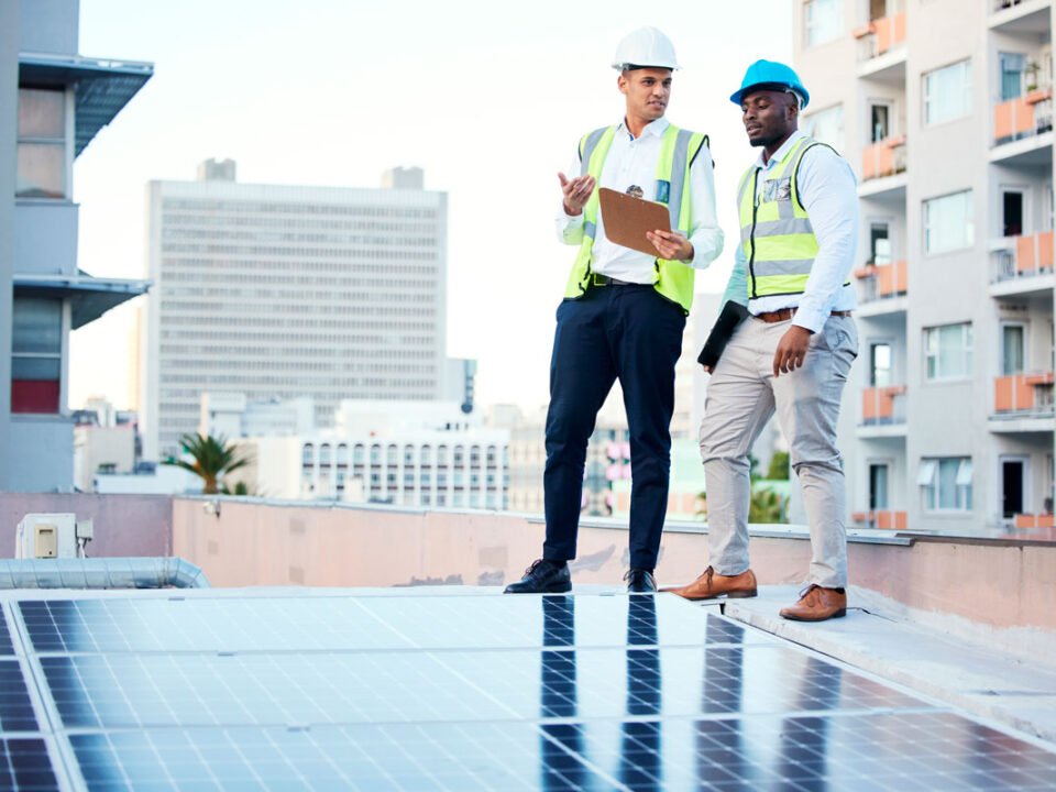 Ingenieros de pie en techo de edificio revisando una instalación de paneles solares.