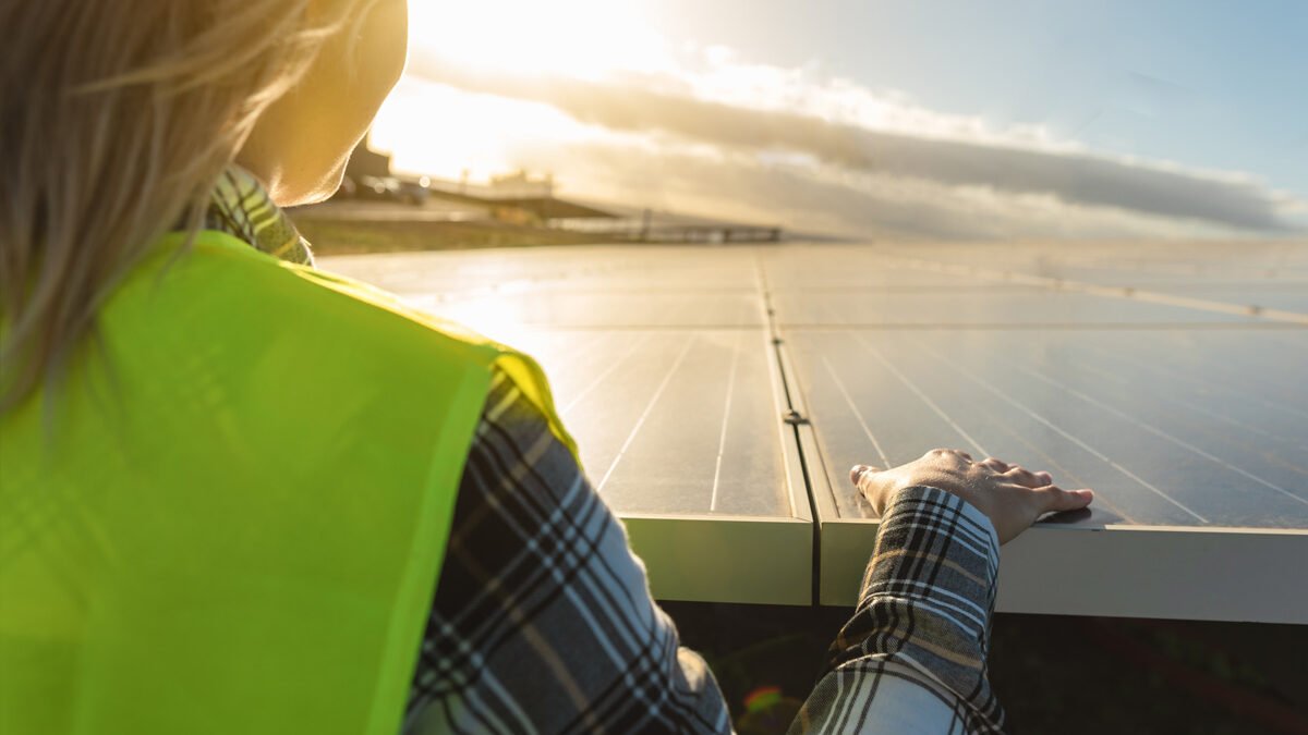Mujer rubia con casco mirando el atardecer en medio de paneles solares
