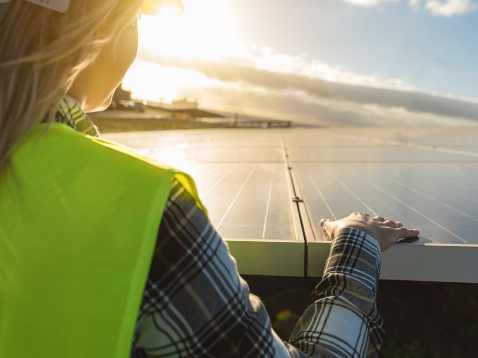 Mujer rubia con casco mirando el atardecer en medio de paneles solares