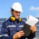 Trabajador en primer plano revisando planilla en el fondo se ven paneles solares y un cielo azul