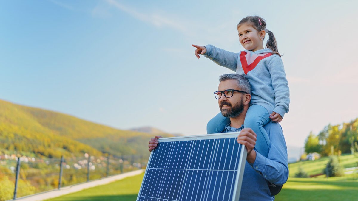 Un padre con su hija sobre sus hombros mirando hacia el futuro, sostiene en la mano un panel solar y en el fondo se ve un campo verde y cielo azul